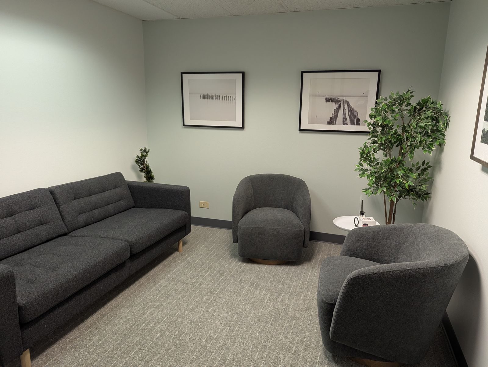 Waiting room with a sofa, two armchairs, a potted tree, and framed black-and-white photographs